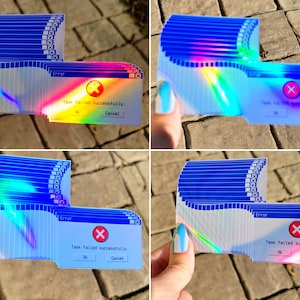 May include: A stack of iridescent blue and white stickers with a holographic finish. Each sticker features a blue and white Windows error message that reads "Task failed successfully." with a red X and "OK" and "Cancel" buttons.