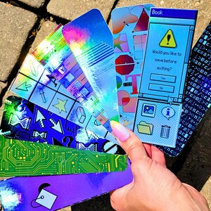 May include: A collection of colorful, holographic bookmarks. Designs include computer interface graphics, circuit board patterns, and geometric shapes. One bookmark features the text "Book" and a prompt: "Would you like to save before exiting?"