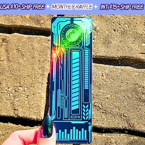 May include: A holographic bookmark with a blue and green color scheme. The bookmark features a circuit board design with a large circle in the center. The bookmark is approximately 2 inches wide and 6 inches long.