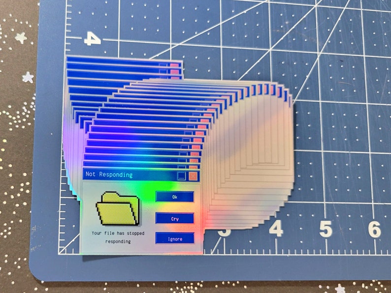 Puede incluir: Una pila de pegatinas hologr&aacute;ficas iridiscentes con un mensaje de error de Windows azul y blanco que dice "No responde" con el texto "Su archivo ha dejado de responder" y botones que dicen "Aceptar", "Llorar" y "Ignorar".