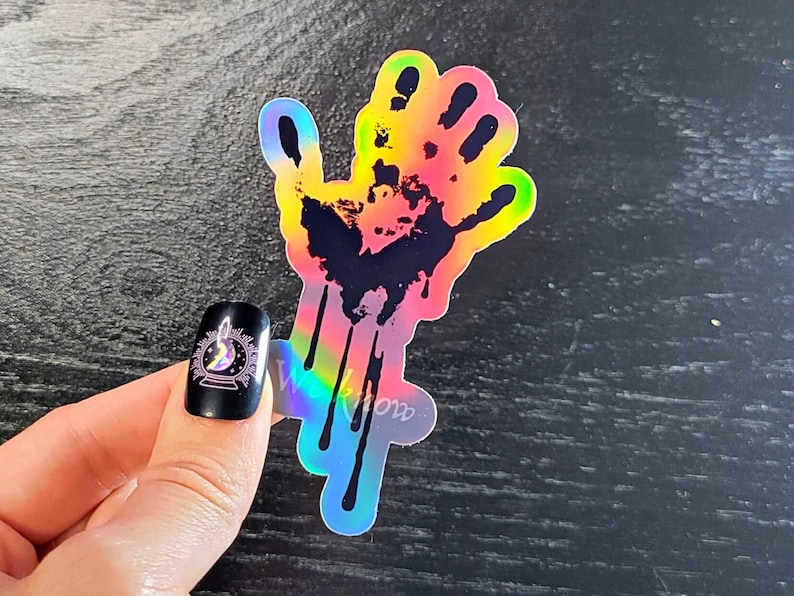 May include: A holographic sticker of a black handprint with dripping blood. The handprint is outlined in rainbow colors.
