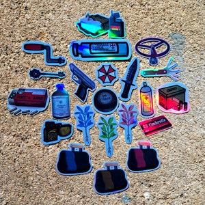 May include: A collection of holographic stickers featuring various designs. Includes a gun, knife, medical supplies, a steering wheel, a key, a red and white umbrella logo, and a duffel bag. The stickers are on a textured, light brown surface.