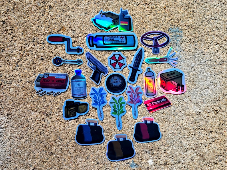 May include: A collection of holographic stickers featuring various designs. Includes a gun, knife, medical supplies, a steering wheel, a key, a red and white umbrella logo, and a duffel bag. The stickers are on a textured, light brown surface.