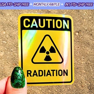 May include: A yellow and black caution sign with a holographic finish. The sign reads "CAUTION RADIATION" and features a black triangular symbol with a stylized radiation symbol inside.