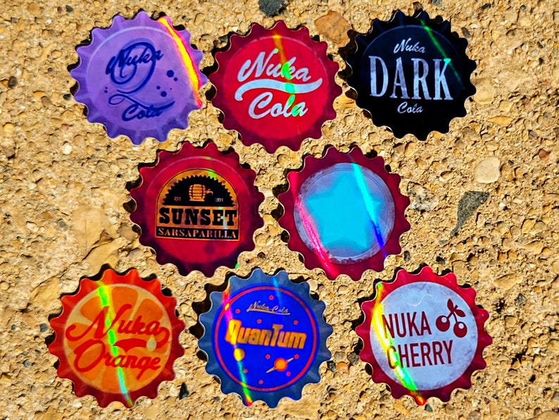 May include: A collection of seven bottle caps with various designs and text. The caps feature the names "Nuka Cola", "Nuka Dark Cola", "Nuka Orange", "Nuka Cherry", "Nuka Quantum", and "Sunset Sarsaparilla". Each cap has a unique color scheme.