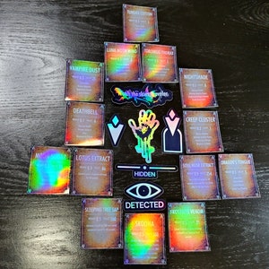 May include: A collection of holographic cards with various names and descriptions. The cards are arranged in a triangular shape on a wooden surface. The cards feature text such as "Tundra Cotton", "Luna Moth Wing", "Vampire Dust", "Deathbell", "Moon Sugar", "Lotus Extract", "Sleeping Tree Sap", "Skooma", "Torchbug Thorax", "Nightshade", "Creep Cluster", "Dragon's Tongue", "Soul Husk Extract", "Frostbite Venom", and "Watch the skies, Traveler."