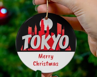 May include: A round Christmas ornament with a black and white design. The ornament features a red silhouette of the Tokyo skyline with the word "TOKYO" in red letters. The bottom of the ornament says "Merry Christmas".