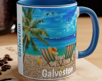 May include: A ceramic mug with a blue interior and handle, featuring a beach scene with palm trees, beach chairs, and the word "Galveston." The mug has a white exterior with the same beach scene.