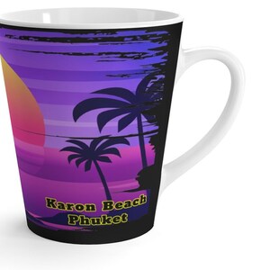 May include: A white ceramic mug with a black background featuring a sunset scene with palm trees and the text "Karon Beach Phuket" in yellow.