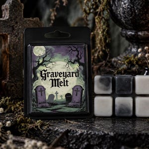May include: A black plastic clamshell package containing wax melts, featuring a label with a graveyard illustration, a full moon, and the text Graveyard Melt. Beside it are six individual square wax cubes in shades of black, grey, and white.