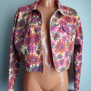 May include: A cropped denim jacket with a floral print in shades of pink, orange, green, and white.