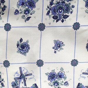 May include: White fabric with a blue and green floral pattern. The fabric features a repeating pattern of flowers and a windmill.