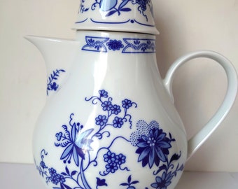 Könnte beinhalten: Eine weiße Porzellan-Kaffeekanne mit blau-weißem Blumenmuster. Die Kanne hat einen Deckel mit einem Knopf oben.