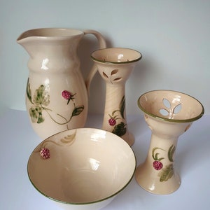 Può includere: Un set di quattro articoli da cucina in ceramica di colore crema con motivi floreali verdi e rosa. Il set comprende una brocca, una ciotola e due portacandele.