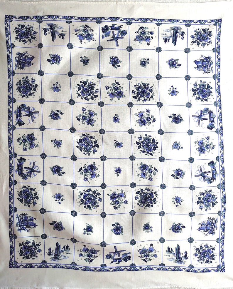 May include: White tablecloth with a blue and white pattern of flowers, windmills, and ships. The pattern is repeated throughout the tablecloth.