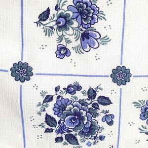 May include: White fabric with a blue and green floral pattern. The pattern features a repeating design of blue flowers with green leaves.