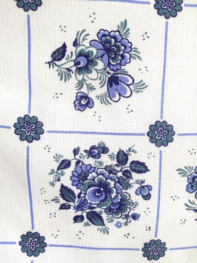 May include: White fabric with a blue and green floral pattern. The pattern features a repeating design of blue flowers with green leaves.