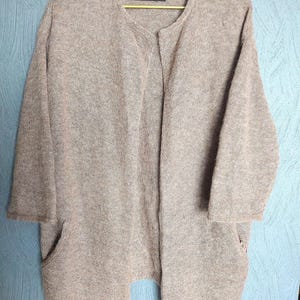 Peut inclure: Un cardigan marron avec une fermeture à bouton unique et deux poches. Le cardigan est fait d'un tissu doux et tricoté. L'étiquette sur le cardigan indique "Made in Scotland".