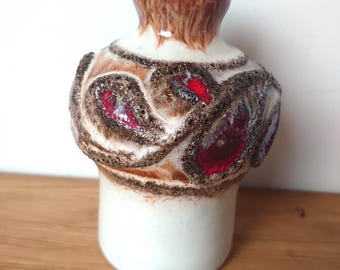 May include: A white ceramic vase with a brown and red geometric design. The vase has a textured surface and a rounded body.