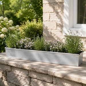 May include: A rectangular galvanised metal planter box with a smooth, silver-toned finish. The container is filled with green foliage and small, delicate light purple flowers, creating a simple and functional display for various plants.