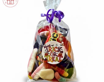 May include: A clear cellophane bag filled with assorted Halloween candies, tied with a purple ribbon. A round sticker with the words "Trick or Treat" and Halloween graphics is attached to the bag. The candies are colorful.