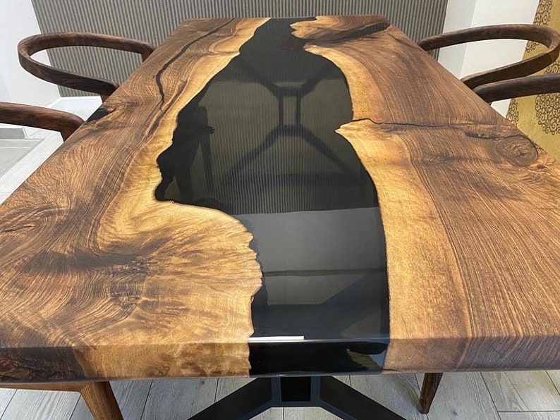 K&ouml;nnte beinhalten: Eine Tischplatte aus Holz mit einem schwarzen Epoxidharzfluss, der durch die Mitte verl&auml;uft. Das Holz hat eine satte braune Farbe und ein nat&uuml;rliches Maserungsmuster. Die Tischplatte ist dick und stabil, und das Harz ist glatt und gl&auml;nzend.