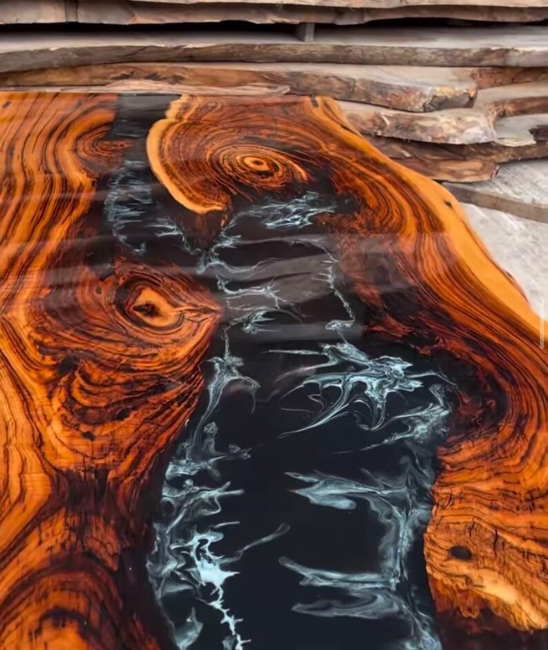 May include: A close-up of a wooden table top with a black and white epoxy resin river running through the center. The wood has a rich, dark brown color with intricate grain patterns.
