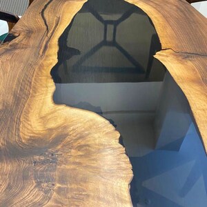 K&ouml;nnte beinhalten: Eine Tischplatte aus Holz mit einer nat&uuml;rlichen Holzmaserung und einem schwarzen Epoxidharzfluss, der durch die Mitte verl&auml;uft.