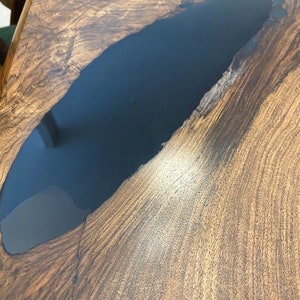 K&ouml;nnte beinhalten: Nahaufnahme einer Tischplatte aus Holz mit einer Einlage aus dunkelblauem Epoxidharz. Das Holz hat eine nat&uuml;rliche Maserung und das Harz ist glatt und gl&auml;nzend.
