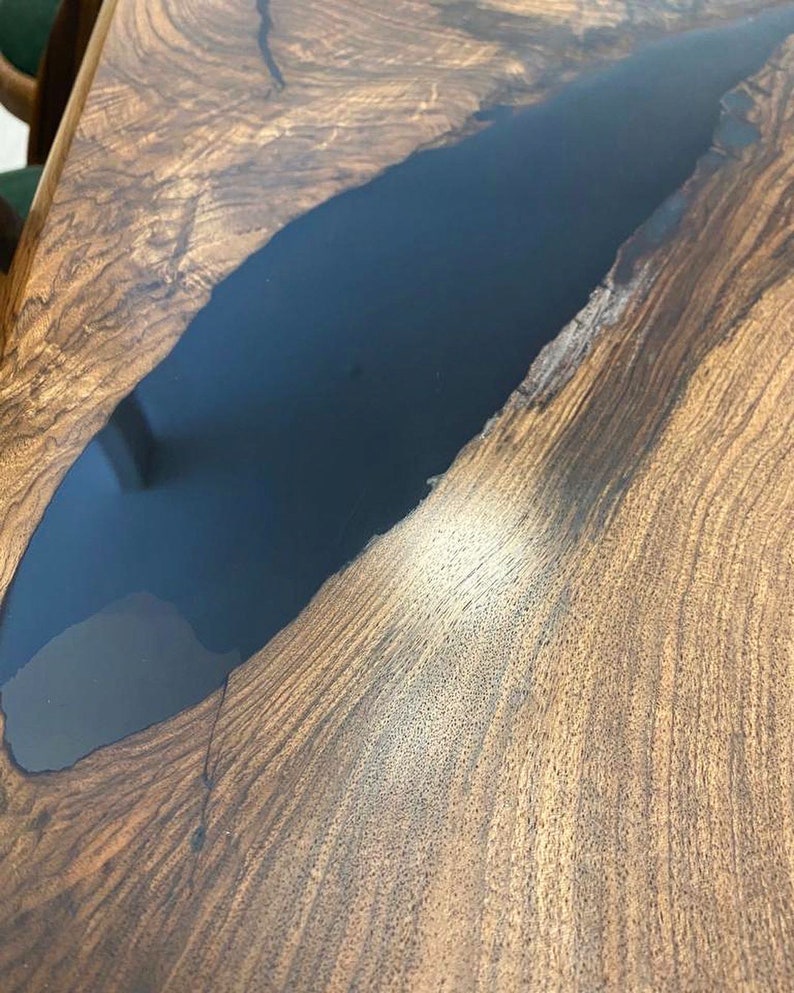 K&ouml;nnte beinhalten: Nahaufnahme einer Tischplatte aus Holz mit einer Einlage aus dunkelblauem Epoxidharz. Das Holz hat eine nat&uuml;rliche Maserung und das Harz ist glatt und gl&auml;nzend.