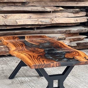 May include: A wooden table with a live edge top and black epoxy resin inlay. The table has a black metal base with an X-shaped design.