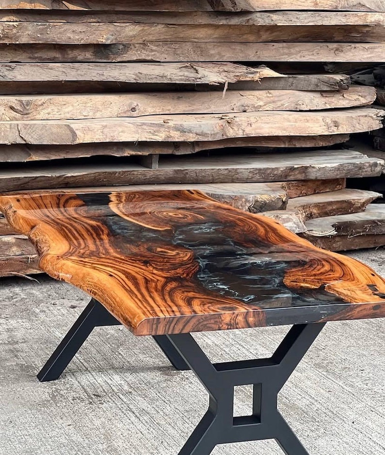 May include: A wooden table with a live edge top and black epoxy resin inlay. The table has a black metal base with an X-shaped design.
