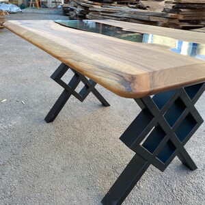 May include: A large wooden table with a live edge top and a black epoxy river running through the center. The table has a black metal base with a geometric design.