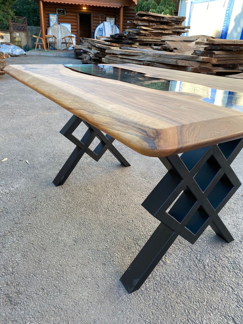May include: A large wooden table with a live edge top and a black epoxy river running through the center. The table has a black metal base with a geometric design.