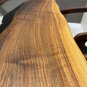 May include: A close-up of a wooden table top with a black epoxy river running through the center. The wood has a rich brown color and a natural grain pattern.