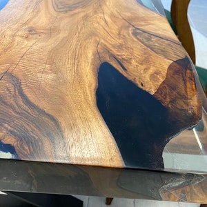 May include: A close-up of a wooden table top with a black epoxy resin inlay. The table top is finished with a clear epoxy resin coating.