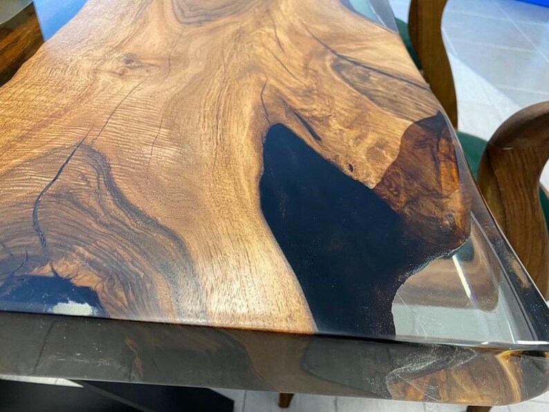 May include: A close-up of a wooden table top with a black epoxy resin inlay. The table top is finished with a clear epoxy resin coating.