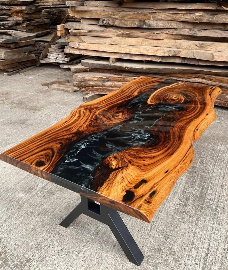 May include: A live edge wood table top with a black and white epoxy river running through the center. The table top is supported by a black metal X-shaped base.