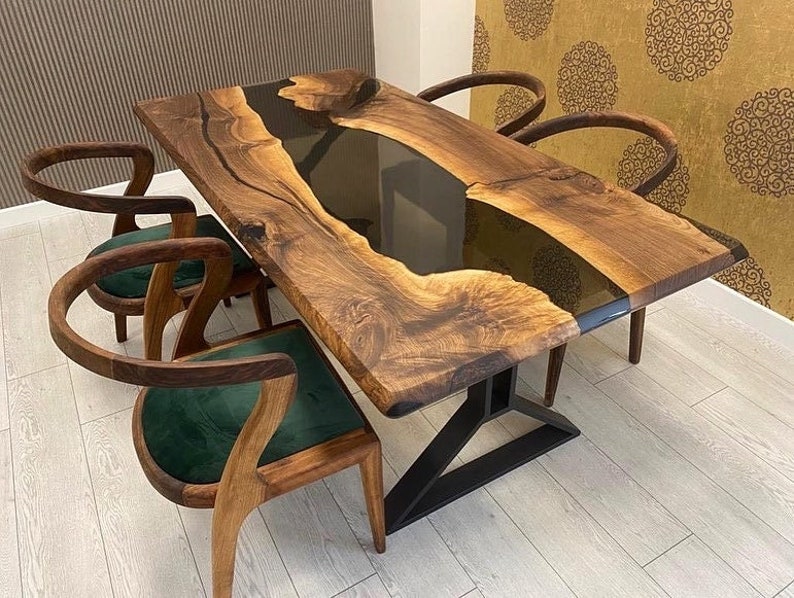 K&ouml;nnte beinhalten: Ein dunkler Holz-Esstisch mit einem schwarzen Epoxidharz-Fluss, der durch die Mitte flie&szlig;t. Der Tisch wird von einem schwarzen Metallgestell getragen und hat vier St&uuml;hle mit gr&uuml;nen Samtsitzen.
