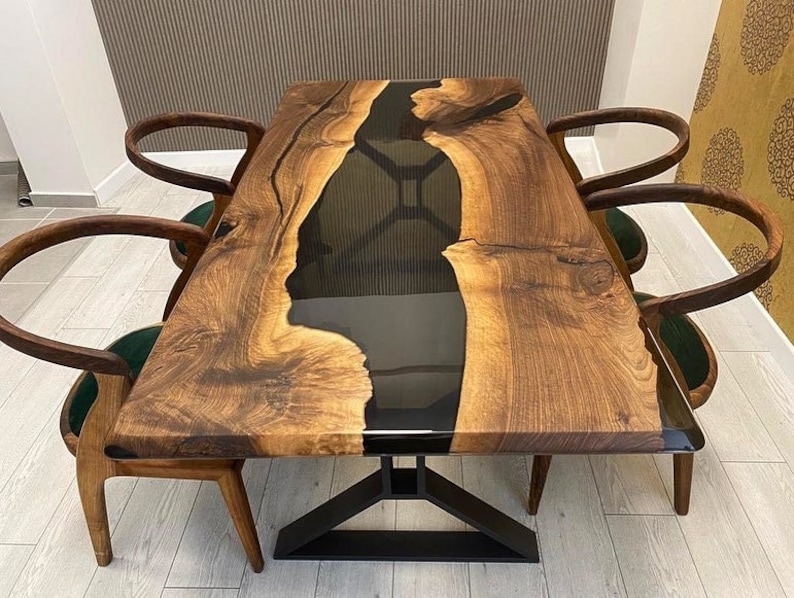K&ouml;nnte beinhalten: Ein dunkler Holz-Esstisch mit einem schwarzen Epoxidharz-Fluss, der durch die Mitte flie&szlig;t. Der Tisch hat ein schwarzes Metallgestell und ist von vier St&uuml;hlen mit dunkelgr&uuml;nen Sitzen umgeben.