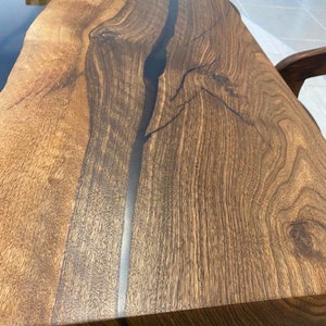 K&ouml;nnte beinhalten: Nahaufnahme einer dunkelbraunen Tischplatte aus Holz mit einem schwarzen Epoxidharzfluss, der durch die Mitte verl&auml;uft. Die Holzmaserung ist sichtbar und die Oberfl&auml;che ist glatt.
