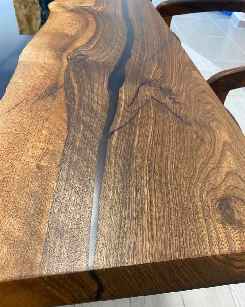 K&ouml;nnte beinhalten: Nahaufnahme einer dunkelbraunen Tischplatte aus Holz mit einem schwarzen Epoxidharzfluss, der durch die Mitte verl&auml;uft. Die Holzmaserung ist sichtbar und die Oberfl&auml;che ist glatt.