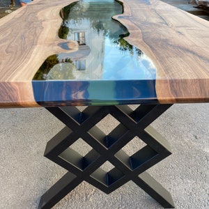 May include: A wooden table with a black epoxy river and a black metal base. The base is a geometric design with a diamond pattern.