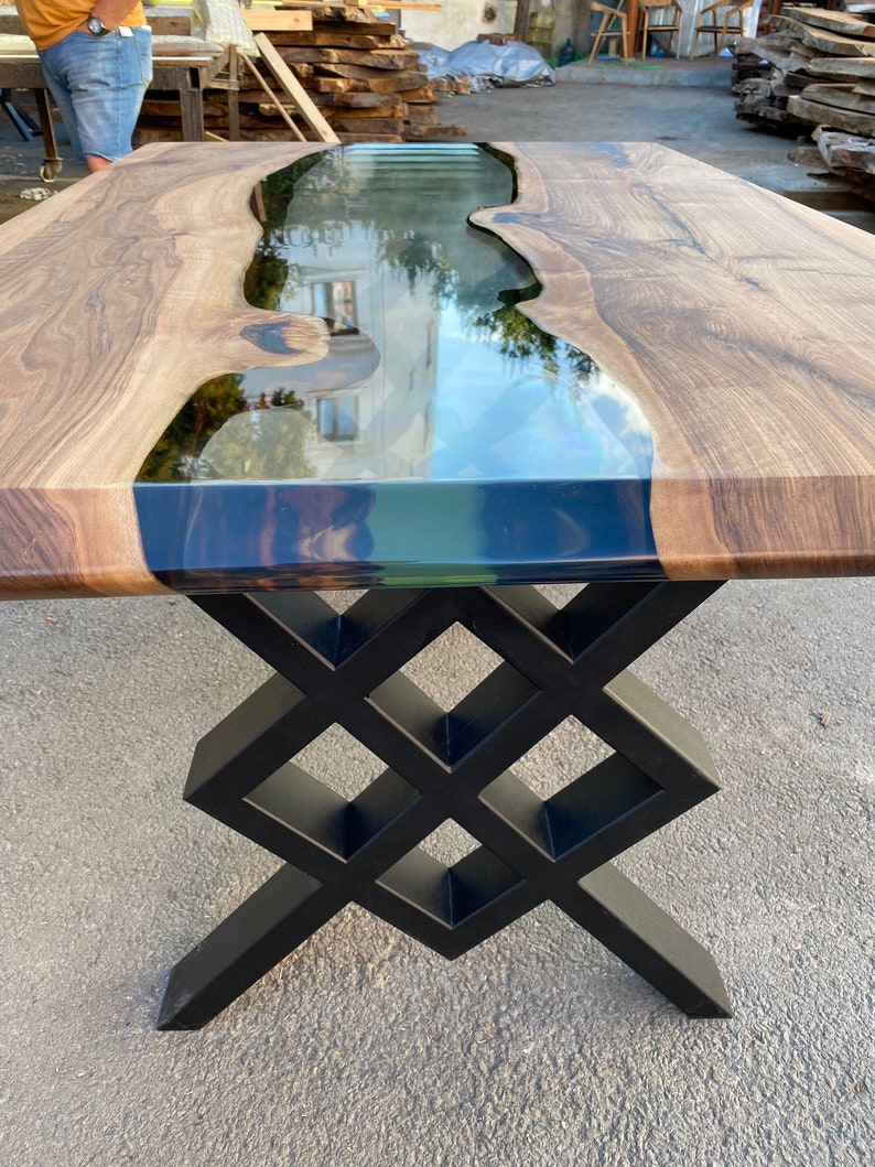 May include: A wooden table with a black epoxy river and a black metal base. The base is a geometric design with a diamond pattern.