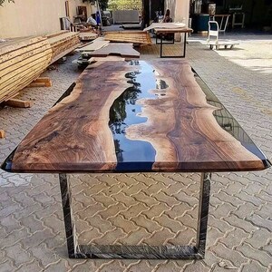Puede incluir: Una mesa de madera grande con un r&iacute;o de resina epoxi negra que atraviesa el centro. La mesa tiene un dise&ntilde;o moderno y minimalista con un marco de metal negro.