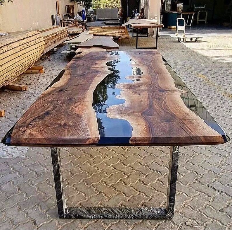 Puede incluir: Una mesa de madera grande con un r&iacute;o de resina epoxi negra que atraviesa el centro. La mesa tiene un dise&ntilde;o moderno y minimalista con un marco de metal negro.