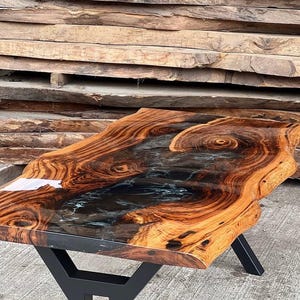 May include: A wooden table with a live edge top and a black epoxy resin inlay. The table has a black metal base.