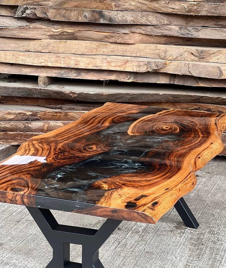 May include: A wooden table with a live edge top and a black epoxy resin inlay. The table has a black metal base.