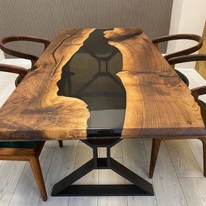 K&ouml;nnte beinhalten: Ein Esstisch aus Holz mit einem schwarzen Epoxidharzfluss, der durch die Mitte verl&auml;uft. Der Tisch hat ein schwarzes Metallgestell und ist von vier St&uuml;hlen mit dunklen Holzrahmen umgeben.