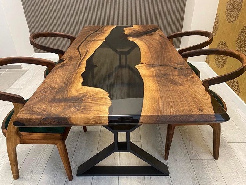 K&ouml;nnte beinhalten: Ein Esstisch aus Holz mit einem schwarzen Epoxidharzfluss, der durch die Mitte verl&auml;uft. Der Tisch hat ein schwarzes Metallgestell und ist von vier St&uuml;hlen mit dunklen Holzrahmen umgeben.